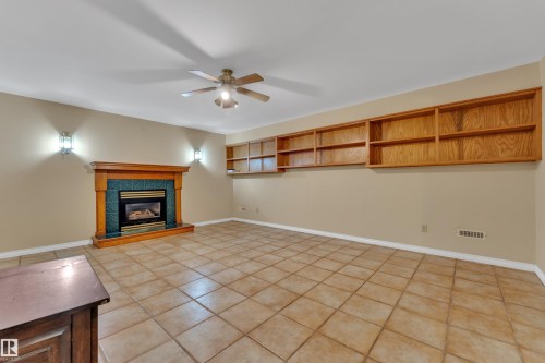 Unfurnished living room featuring a ceiling fan, a fireplace, and light tile patterned flooring - 20920 9 Avenue, Edmonton, AB - Indoor With Fireplace