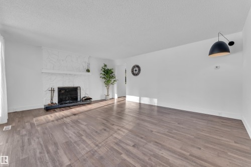 Unfurnished living room featuring a stone fireplace, wood finished floors, and a textured ceiling - 20920 9 Avenue, Edmonton, AB - Indoor Photo Showing Living Room With Fireplace