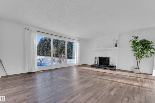 Unfurnished living room featuring a textured ceiling, wood finished floors, and a high end fireplace - 20920 9 Avenue, Edmonton, AB - Indoor Photo Showing Living Room With Fireplace