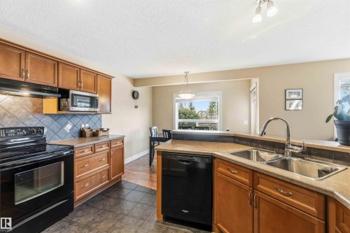 Kitchen featuring black appliances, wood finish cabinetry, pendant lighting, decorative backsplash, and a textured ceiling - 11715 167A Avenue, Edmonton, AB - Indoor Photo Showing Kitchen With Double Sink