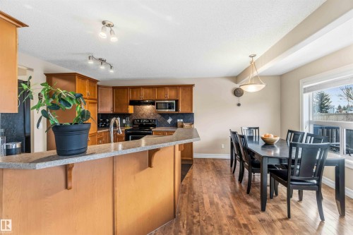 Kitchen with wood finish cabinetry, a breakfast bar, pendant lighting, black range with electric cooktop, and dark wood-style flooring - 11715 167A Avenue, Edmonton, AB - Indoor