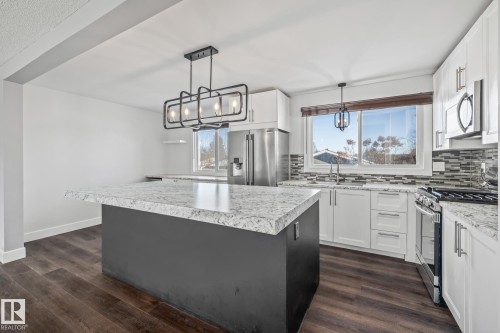 Dual tone kitchen featuring stainless steel appliances, decorative backsplash, a kitchen island, dark wood-style flooring, and two tone color scheme - 14911 96 Street, Edmonton, AB - Indoor Photo Showing Kitchen With Upgraded Kitchen