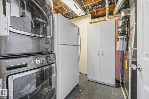 Laundry area with concrete floors, stacked washer and dryer, and heating unit - 14911 96 Street, Edmonton, AB - Indoor Photo Showing Laundry Room
