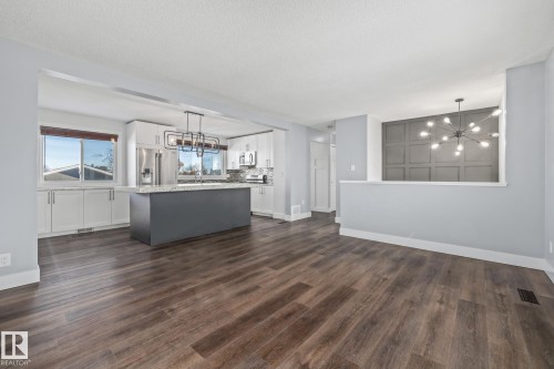 Two tone kitchen with a chandelier, a center island, two tone color scheme, dark wood finished floors, and stainless steel microwave - 14911 96 Street, Edmonton, AB - Indoor