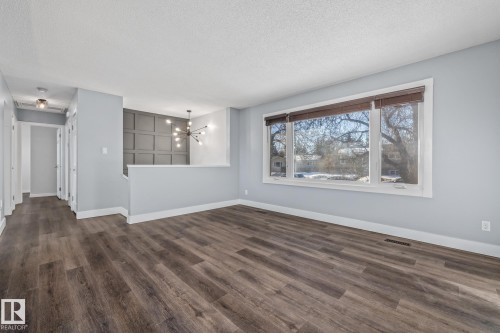 Empty room with a chandelier, a textured ceiling, and dark wood-style floors - 14911 96 Street, Edmonton, AB - Indoor