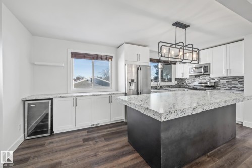 Two tone kitchen with light countertops, two tone cabinets, beverage cooler, stainless steel appliances, and a kitchen island - 14911 96 Street, Edmonton, AB - Indoor Photo Showing Kitchen With Upgraded Kitchen