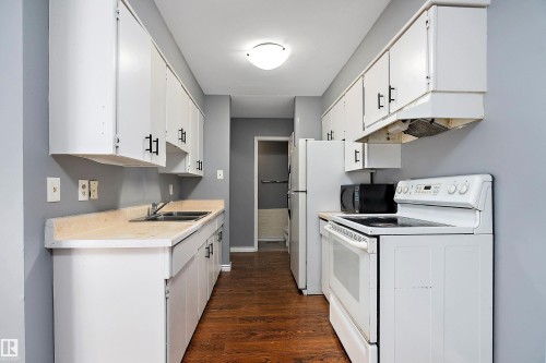 Kitchen with white appliances, light countertops, dark wood-style floors, and white cabinetry - 15C Callingwood Crest, Edmonton, AB - Indoor Photo Showing Kitchen With Double Sink