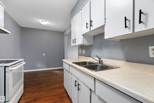 Kitchen featuring light countertops, white range with electric cooktop, white cabinets, and dark wood finished floors - 15C Callingwood Crest, Edmonton, AB - Indoor Photo Showing Kitchen With Double Sink