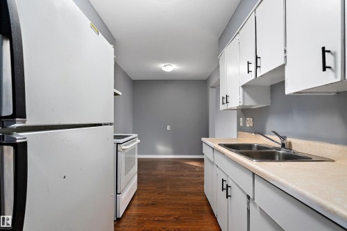 Kitchen with freestanding refrigerator, light countertops, electric stove, dark wood-type flooring, and white cabinetry - 15C Callingwood Crest, Edmonton, AB - Indoor Photo Showing Kitchen With Double Sink