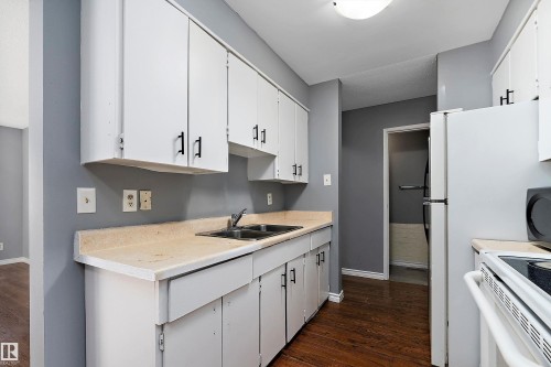 Kitchen with light countertops, white cabinets, dark wood-style flooring, and white appliances - 15C Callingwood Crest, Edmonton, AB - Indoor Photo Showing Kitchen With Double Sink