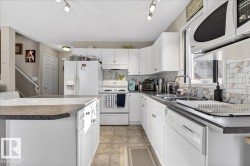 Kitchen featuring white appliances, dark countertops, white cabinetry, track lighting, and a kitchen island - 