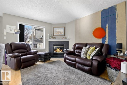Living room with wood finished floors, a textured ceiling, and a tiled fireplace - 23 4020 21 Street, Edmonton, AB - Indoor Photo Showing Living Room With Fireplace
