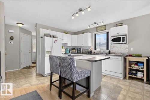 Kitchen featuring a breakfast bar, white appliances, tasteful backsplash, a center island, and white cabinets - 23 4020 21 Street, Edmonton, AB - Indoor Photo Showing Kitchen