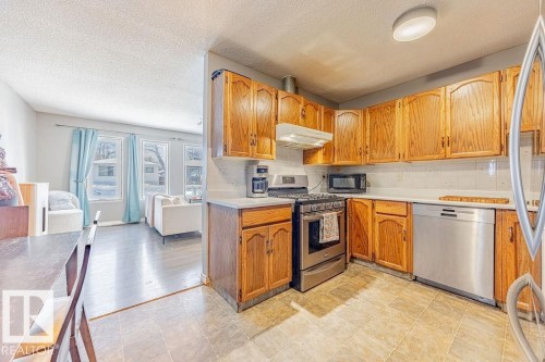 Kitchen featuring stainless steel appliances, light countertops, a textured ceiling, under cabinet range hood, and tasteful backsplash - 12253 95A Street, Edmonton, AB - Indoor Photo Showing Kitchen
