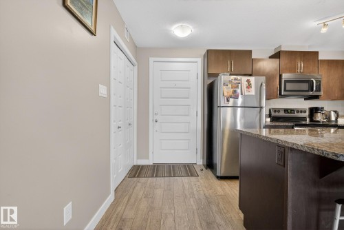 Kitchen with stainless steel appliances, dark stone countertops, light wood-type flooring, and dark wood finish cabinetry - 104 8515 99 Street, Edmonton, AB - Indoor Photo Showing Kitchen