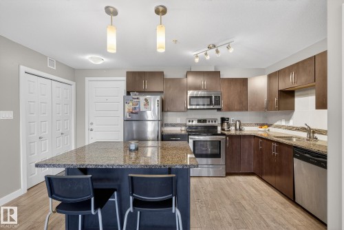 Kitchen with dark stone counters, stainless steel appliances, dark wood finish cabinets, and light wood-style floors - 104 8515 99 Street, Edmonton, AB - Indoor Photo Showing Kitchen With Double Sink