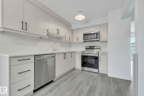 Kitchen with stainless steel appliances, light wood finished floors, a textured ceiling, decorative backsplash, and light stone counters - 1281 Hooke Road, Edmonton, AB - Indoor Photo Showing Kitchen