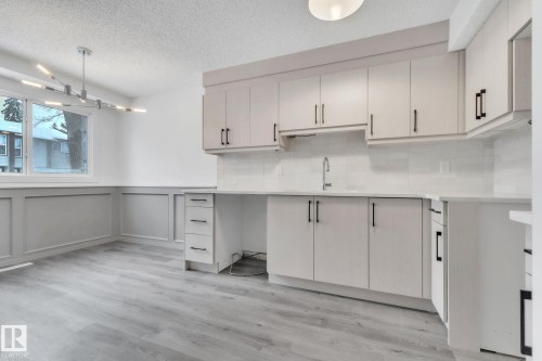 Kitchen featuring a textured ceiling, light wood-type flooring, suspended lighting, tasteful backsplash, and wainscoting - 1281 Hooke Road, Edmonton, AB - Indoor Photo Showing Kitchen