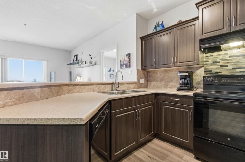 Kitchen with black appliances, dark wood finish cabinetry, light countertops, light wood finished floors, and backsplash - 313 263 Macewan Road, Edmonton, AB - Indoor Photo Showing Kitchen With Double Sink