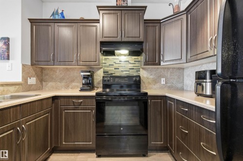 Kitchen featuring black appliances, light countertops, extractor fan, tasteful backsplash, and dark wood finish cabinetry - 313 263 Macewan Road, Edmonton, AB - Indoor Photo Showing Kitchen
