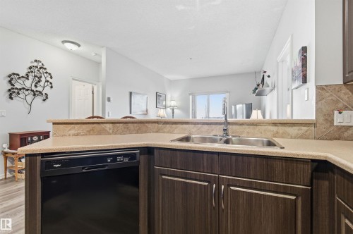 Kitchen with dark wood finish cabinets, dishwasher, light countertops, tasteful backsplash, and a peninsula - 313 263 Macewan Road, Edmonton, AB - Indoor Photo Showing Kitchen With Double Sink