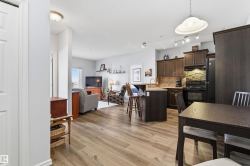 Kitchen featuring light countertops, a breakfast bar area, dark wood finish cabinets, black appliances, and light wood-style flooring - 313 263 Macewan Road, Edmonton, AB - Indoor