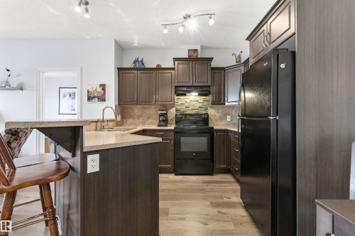 Kitchen featuring black appliances, dark wood finish cabinetry, a breakfast bar area, light wood-style floors, and a peninsula - 313 263 Macewan Road, Edmonton, AB - Indoor Photo Showing Kitchen With Upgraded Kitchen
