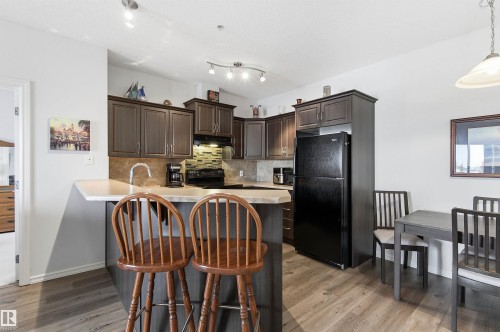 Kitchen with dark wood finish cabinets, light countertops, black appliances, backsplash, and light wood-style floors - 313 263 Macewan Road, Edmonton, AB - Indoor
