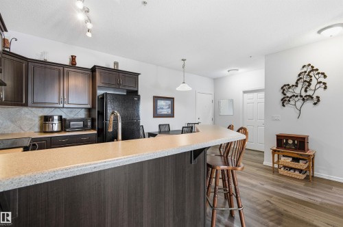 Kitchen featuring dark wood finish cabinetry, black appliances, hanging light fixtures, backsplash, and dark wood finished floors - 313 263 Macewan Road, Edmonton, AB - Indoor Photo Showing Kitchen With Upgraded Kitchen