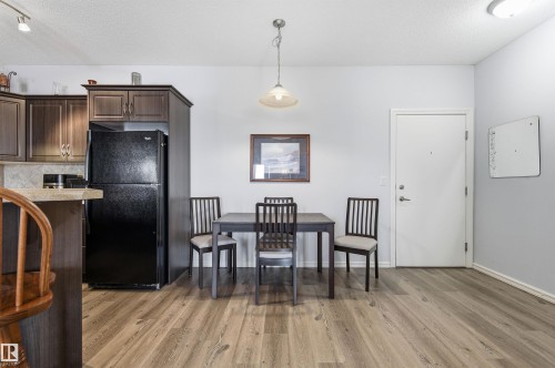 Kitchen with freestanding refrigerator, decorative light fixtures, light countertops, dark wood finish cabinets, and a textured ceiling - 313 263 Macewan Road, Edmonton, AB - Indoor Photo Showing Kitchen
