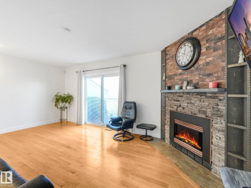 Living area featuring wood finished floors and a large fireplace - 61 9520 174 Street, Edmonton, AB - Indoor Photo Showing Living Room With Fireplace