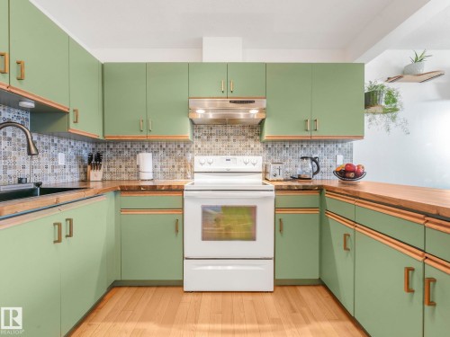 Kitchen with electric range, green cabinets, light wood finished floors, and backsplash - 61 9520 174 Street, Edmonton, AB - Indoor Photo Showing Kitchen