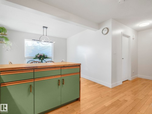 Kitchen featuring green cabinetry, light wood finished floors, beam ceiling, light countertops, and hanging lights - 61 9520 174 Street, Edmonton, AB - Indoor