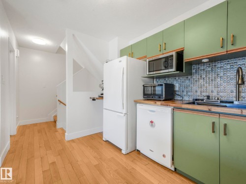Kitchen featuring green cabinetry, white appliances, light wood finished floors, tasteful backsplash, and wood counters - 61 9520 174 Street, Edmonton, AB - Indoor Photo Showing Kitchen