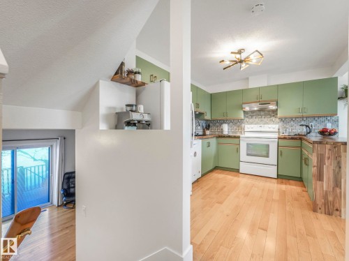 Kitchen with green cabinetry, white appliances, light wood-style floors, a textured ceiling, and decorative backsplash - 61 9520 174 Street, Edmonton, AB - Indoor Photo Showing Kitchen
