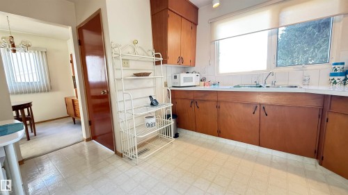 Kitchen with wood finish cabinets, light floors, light countertops, white microwave, and hanging lights - 4608 102 Avenue, Edmonton, AB - Indoor Photo Showing Kitchen With Double Sink