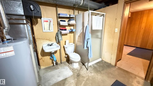 Bathroom with wooden walls, unfinished concrete flooring, water heater, and a stall shower - 4608 102 Avenue, Edmonton, AB - Indoor Photo Showing Basement
