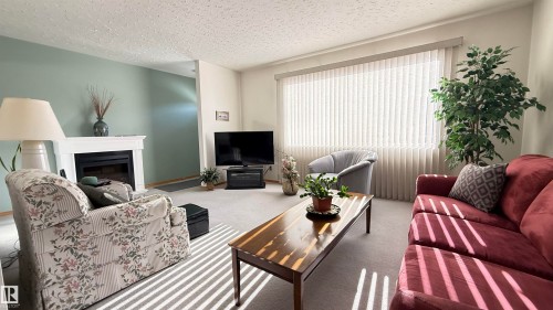 Carpeted living area featuring a textured ceiling and a fireplace - 4608 102 Avenue, Edmonton, AB - Indoor Photo Showing Living Room With Fireplace
