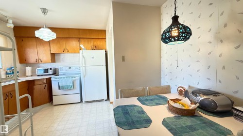 Kitchen featuring white appliances, light countertops, light flooring, wood finish cabinets, and decorative light fixtures - 4608 102 Avenue, Edmonton, AB - Indoor Photo Showing Kitchen