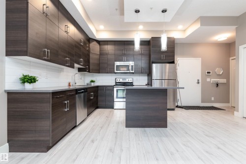 Kitchen with dark wood finish cabinetry, stainless steel appliances, light countertops, pendant lighting, and a center island - 105 10006 83 Avenue, Edmonton, AB - Indoor Photo Showing Kitchen With Stainless Steel Kitchen With Upgraded Kitchen