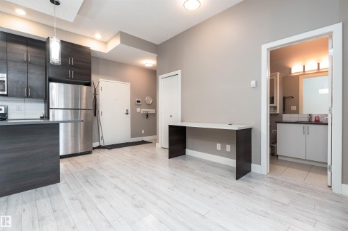 Kitchen featuring stainless steel appliances, modern cabinets, hanging light fixtures, light wood-style floors, and dark wood finish cabinets - 105 10006 83 Avenue, Edmonton, AB - Indoor Photo Showing Kitchen