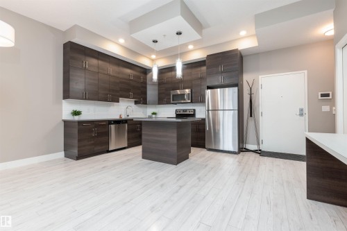 Kitchen featuring dark wood finish cabinetry, stainless steel appliances, modern cabinets, and light countertops - 105 10006 83 Avenue, Edmonton, AB - Indoor Photo Showing Kitchen With Stainless Steel Kitchen