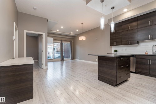 Kitchen featuring dark wood finish cabinetry, open floor plan, pendant lighting, a kitchen island, and light wood-type flooring - 105 10006 83 Avenue, Edmonton, AB - Indoor Photo Showing Kitchen