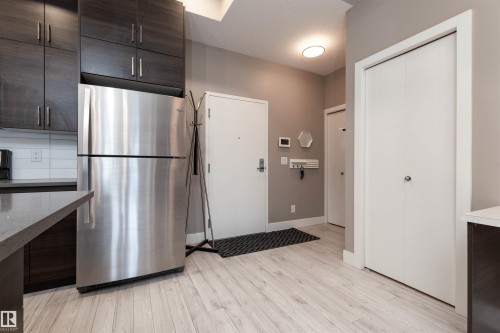 Kitchen featuring dark wood finish cabinetry, freestanding refrigerator, light wood-type flooring, and modern cabinets - 105 10006 83 Avenue, Edmonton, AB - Indoor Photo Showing Kitchen With Stainless Steel Kitchen