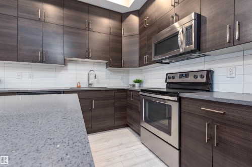 Kitchen with stainless steel appliances, dark wood finish cabinetry, tasteful backsplash, and light stone countertops - 105 10006 83 Avenue, Edmonton, AB - Indoor Photo Showing Kitchen With Stainless Steel Kitchen With Upgraded Kitchen