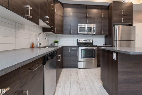 Kitchen featuring stainless steel appliances, dark wood finish cabinetry, and dark stone counters - 105 10006 83 Avenue, Edmonton, AB - Indoor Photo Showing Kitchen With Stainless Steel Kitchen With Upgraded Kitchen