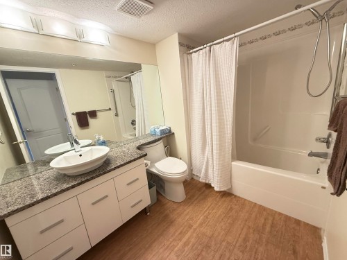 Bathroom with vanity, a textured ceiling, light wood-style floors, and shower / bath combo with shower curtain - 302 8215 84 Avenue, Edmonton, AB - Indoor Photo Showing Bathroom