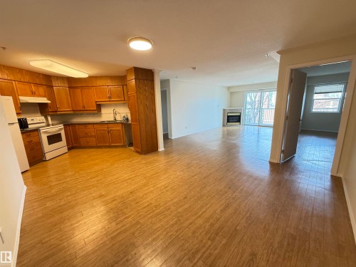 Kitchen with dark countertops, wood finish cabinets, white appliances, light wood finished floors, and open floor plan - 302 8215 84 Avenue, Edmonton, AB - Indoor Photo Showing Kitchen