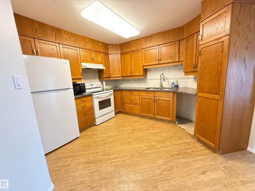Kitchen featuring wood finish cabinets, white appliances, light wood-type flooring, a textured ceiling, and tasteful backsplash - 302 8215 84 Avenue, Edmonton, AB - Indoor Photo Showing Kitchen