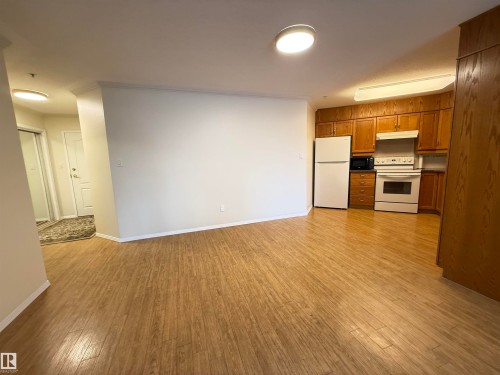 Kitchen with wood finish cabinets, white appliances, light wood finished floors, and crown molding - 302 8215 84 Avenue, Edmonton, AB - Indoor Photo Showing Kitchen